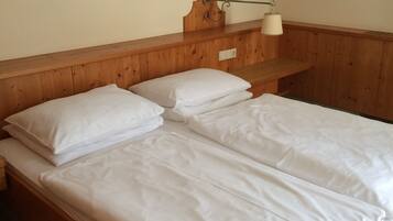 Una cama litera de madera con ropa blanca en una habitación con techo inclinado y cabecera de madera.