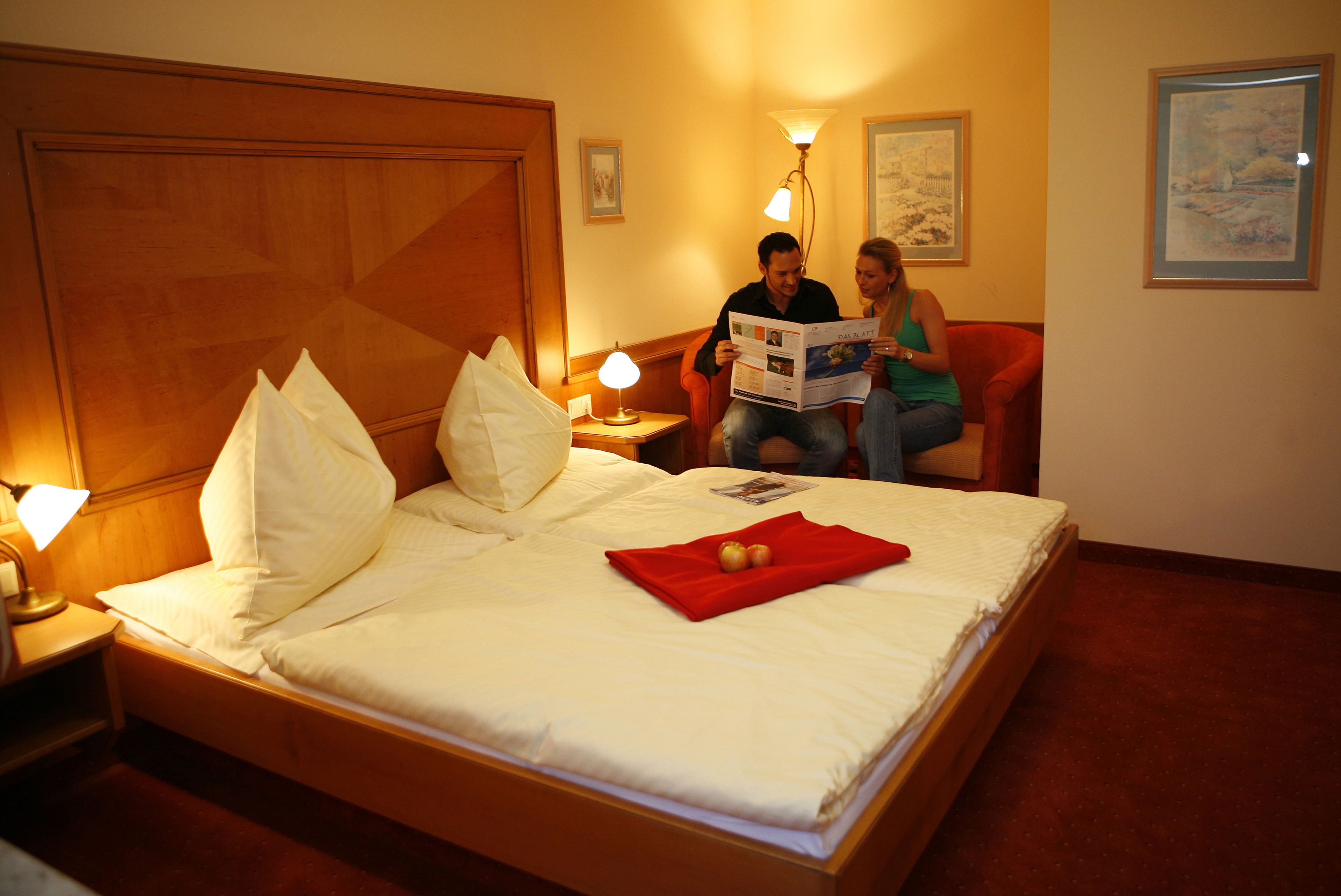 Quarto de hotel com uma cama grande, duas luminárias de cabeceira, uma cabeceira de madeira e um cobertor vermelho.