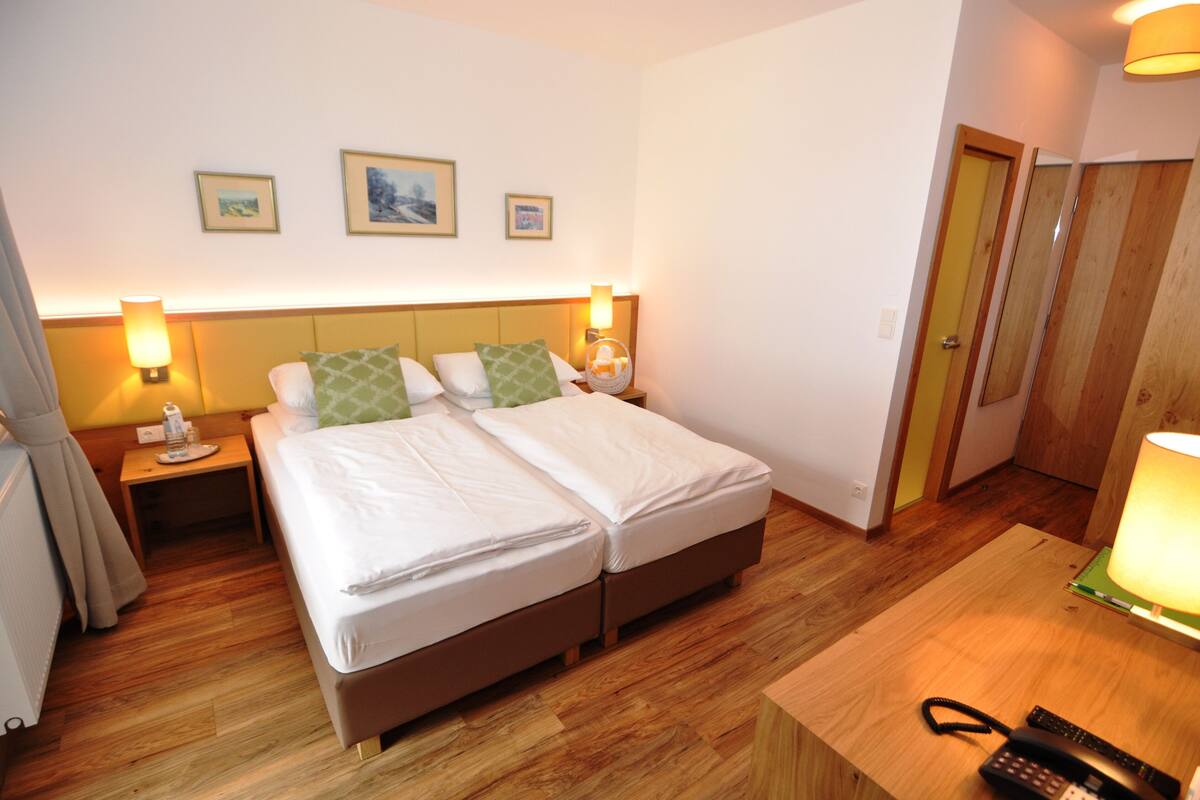 A double bed with two pillows, a bedside table with a lamp, and a wooden floor.