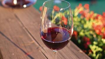 A wine glass filled with red wine on a wooden surface with a blurred background of greenery and flowers.