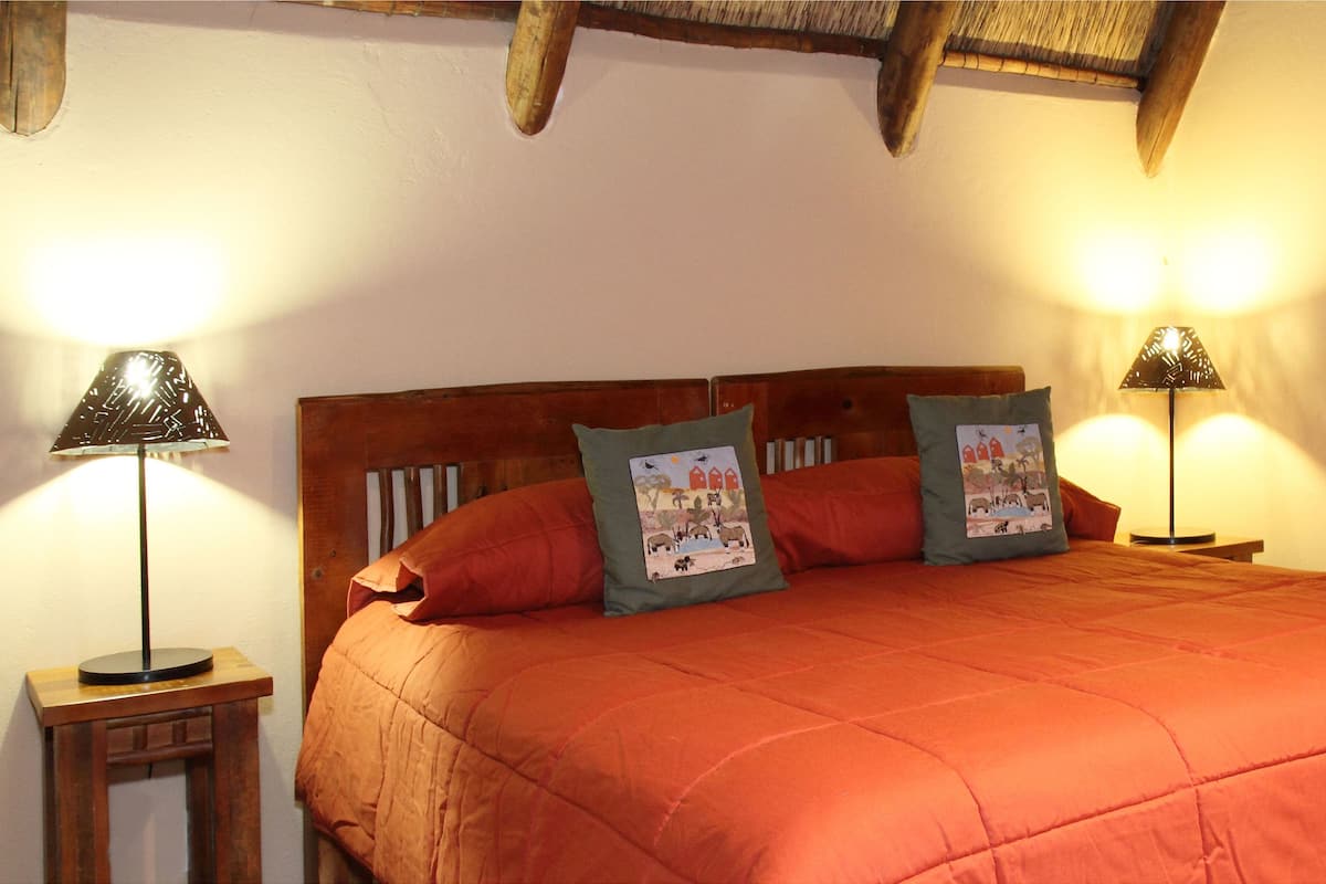 A bed with an orange bedspread, two pillows with illustrations, and two table lamps on wooden nightstands.