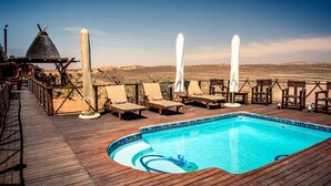 A wooden deck with a swimming pool, lounge chairs, and a thatched-roof structure. - Xaus Lodge (Mier)