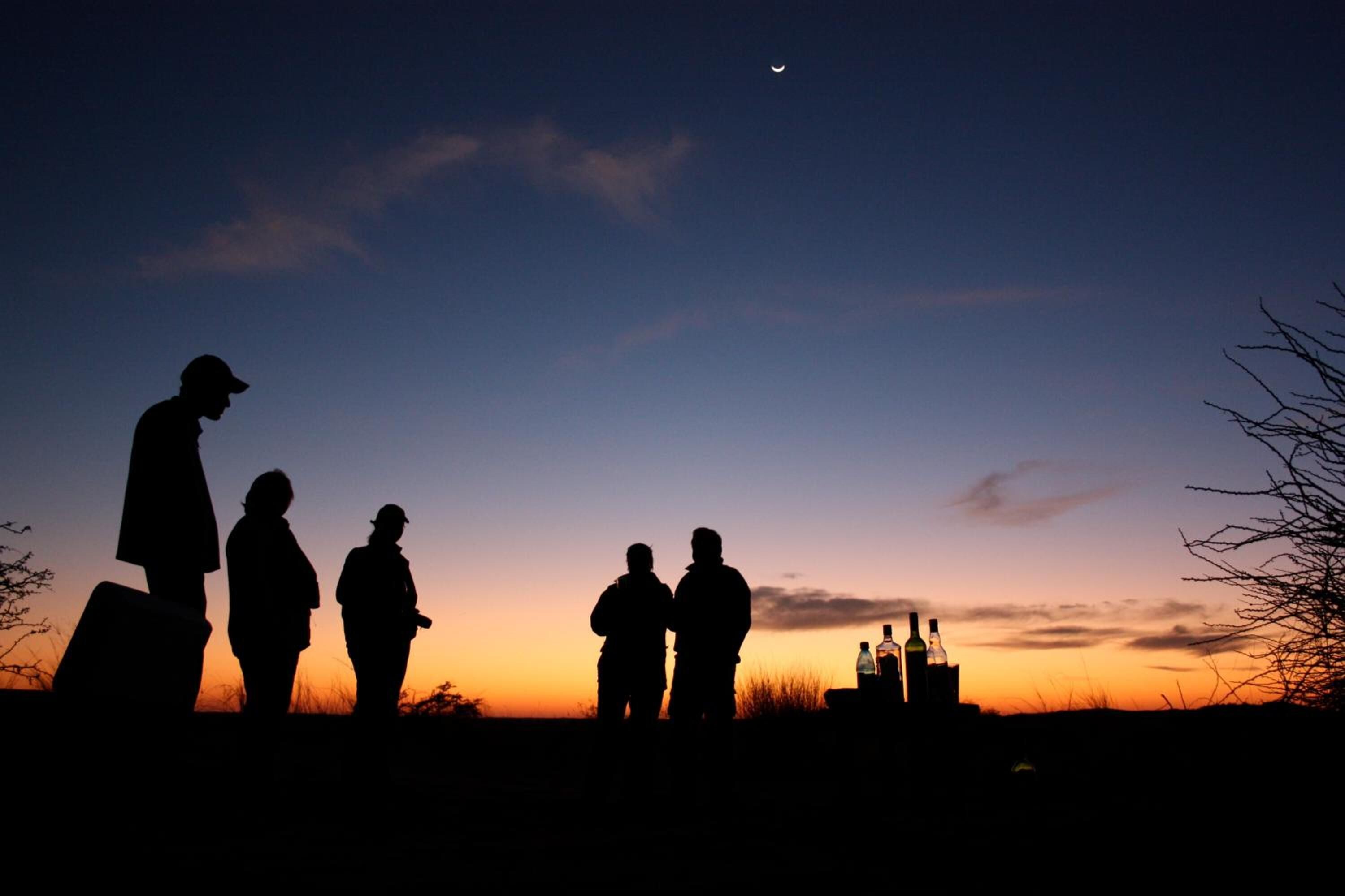 Silhuetas de pessoas contra um céu ao pôr do sol.