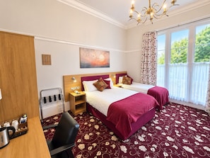 A hotel room with two beds, a desk with a kettle, a chair, a painting on the wall, and a large window with curtains. - Edgerton Hotel (Huddersfield)