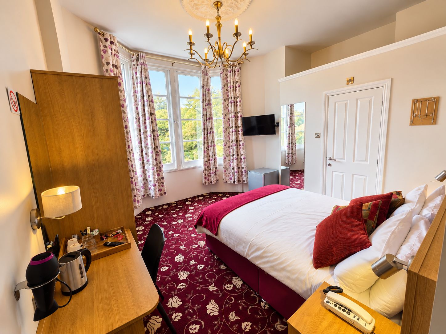 Une chambre d’hôtel équipée d’un lit, d’un bureau, d’une chaise, d’un téléphone, d’une télévision et d’un lustre.