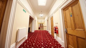 A hallway with a red carpet, wooden doors, a radiator, and a chandelier. - Edgerton Hotel (Huddersfield)