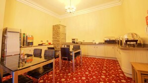A hotel room with a dining area featuring a glass table, black chairs, a red patterned carpet, a stone pillar, a kitchenette with a coffee machine, and a ceiling light fixture. - Edgerton Hotel (Huddersfield)