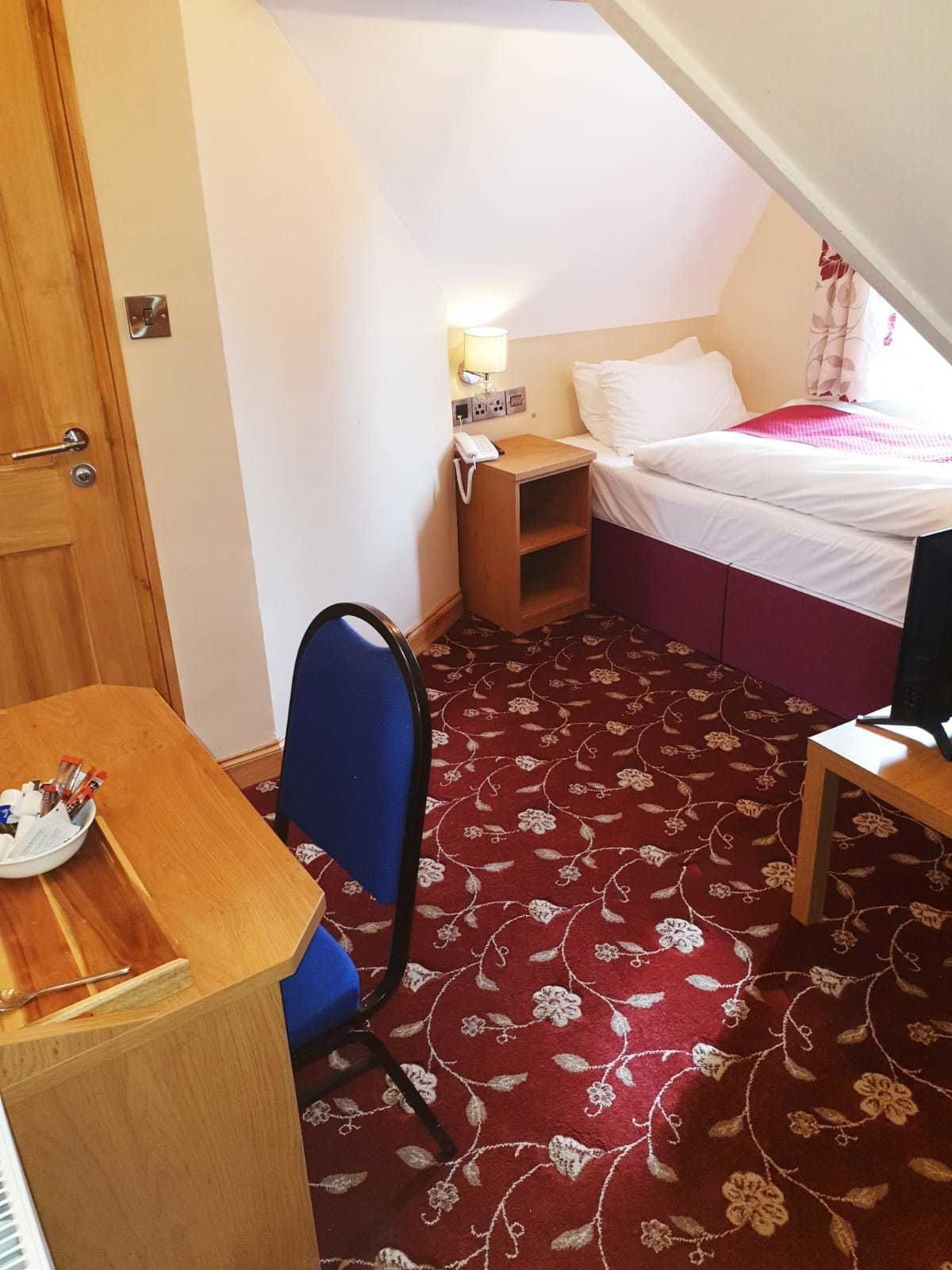 Una habitación pequeña y funcional con cama, escritorio, silla y piso alfombrado.