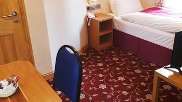 Una habitación pequeña y funcional con cama, escritorio, silla y piso alfombrado.