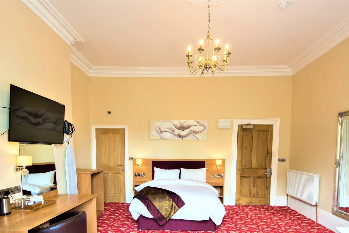 Habitación de hotel con una cama grande, un televisor de pantalla plana, un escritorio de madera y un candelabro.
