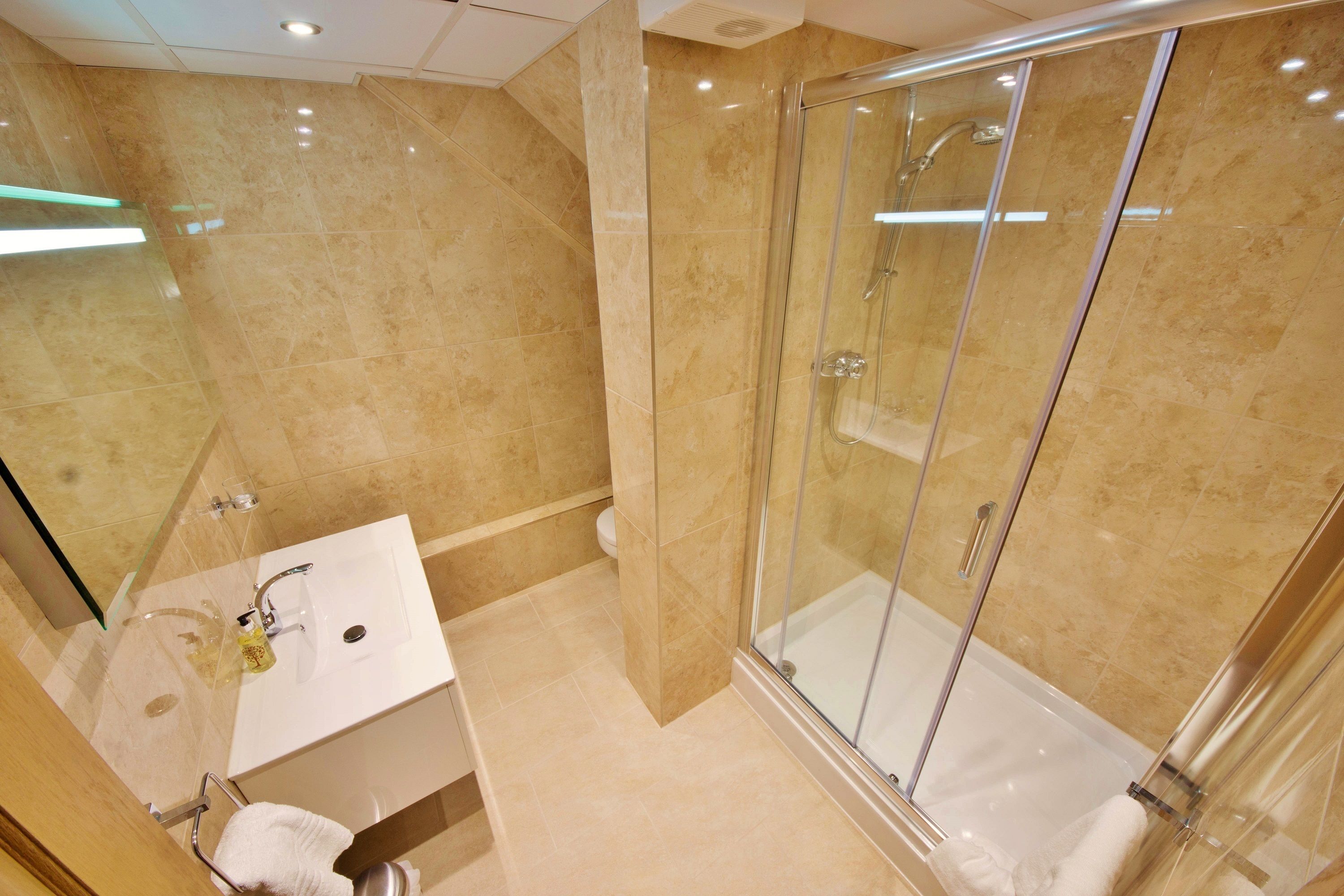 Un baño moderno con ducha acristalada, lavamanos blanco y espejo.