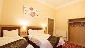 A hotel room with two beds, a wooden wardrobe, a coat rack, and a painting on the wall.