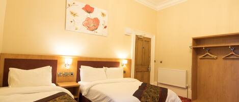 A hotel room with two beds, a wooden wardrobe, a coat rack, and a painting on the wall.