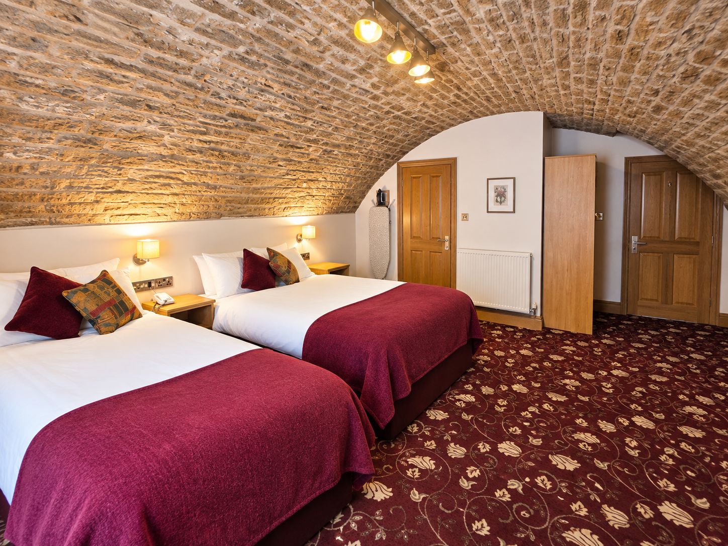 A room with two beds, a stone ceiling, a radiator, and a wooden wardrobe.