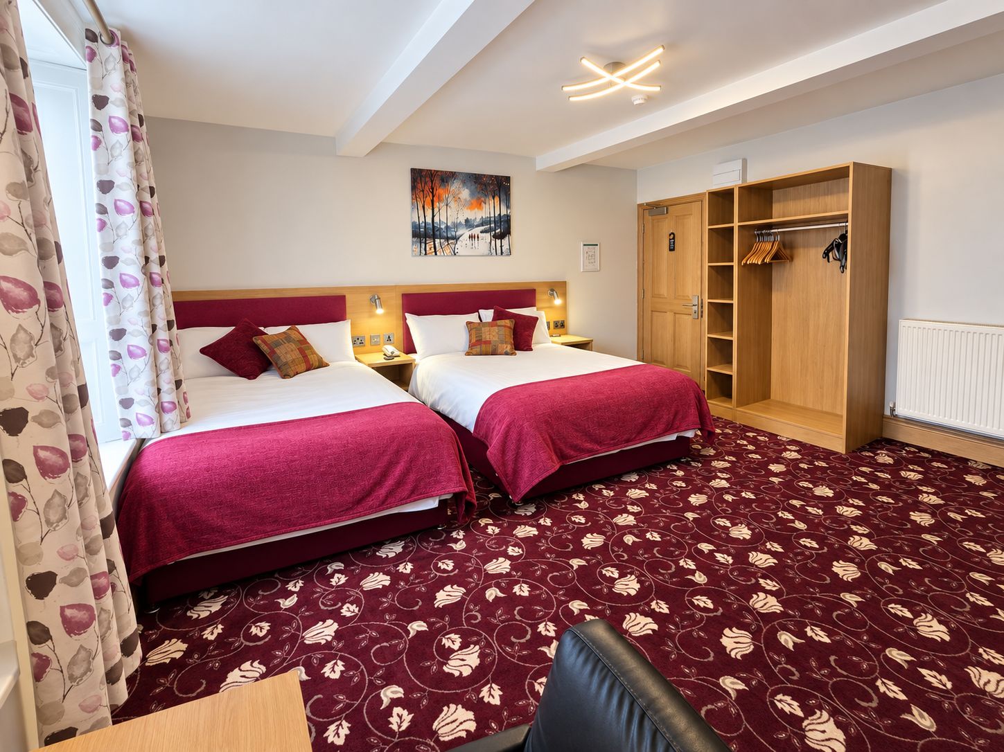 A hotel room with two beds, a wardrobe, a desk, and a painting on the wall.