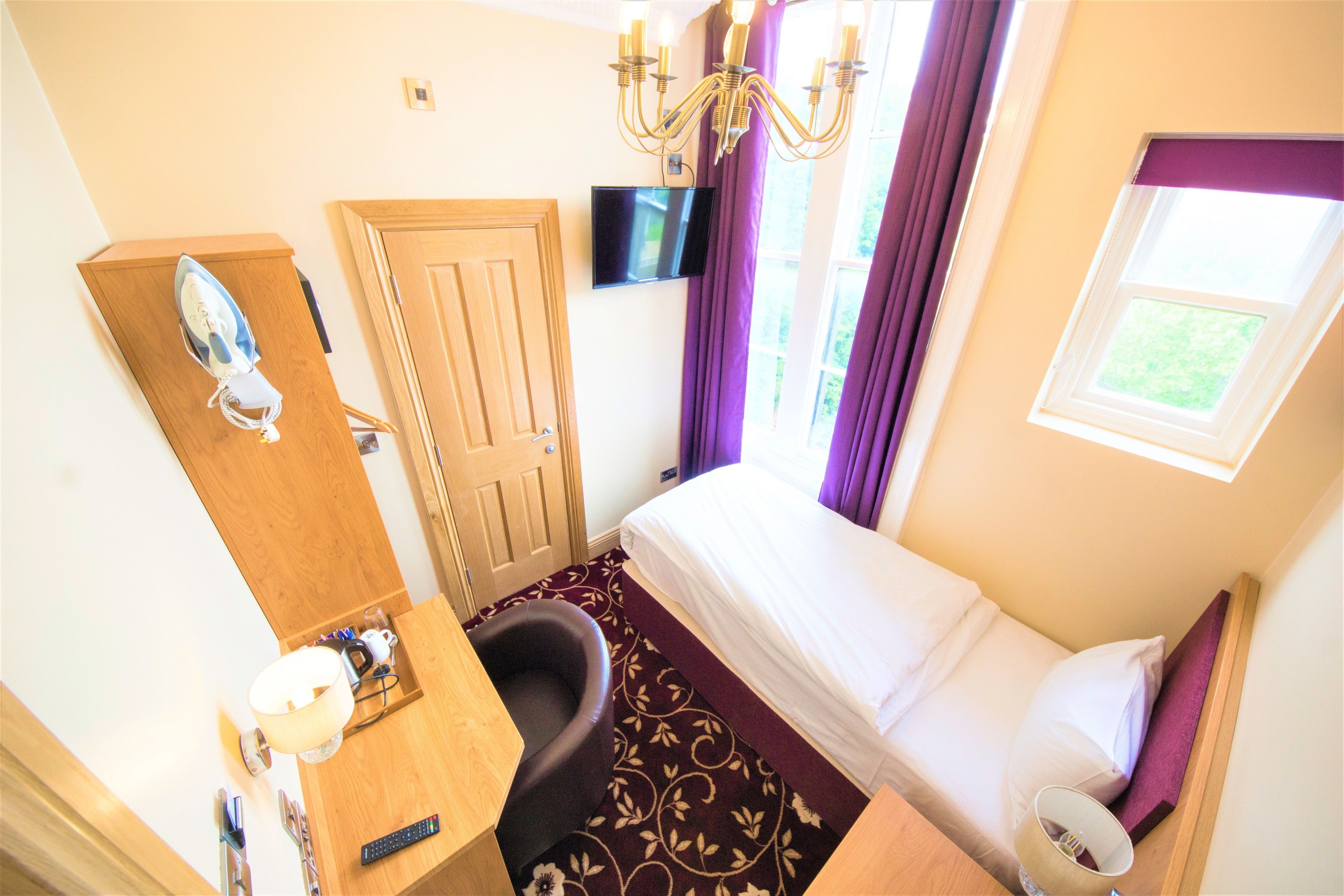 A hotel room with a bed, a desk, a chair, a TV, and a window with curtains.