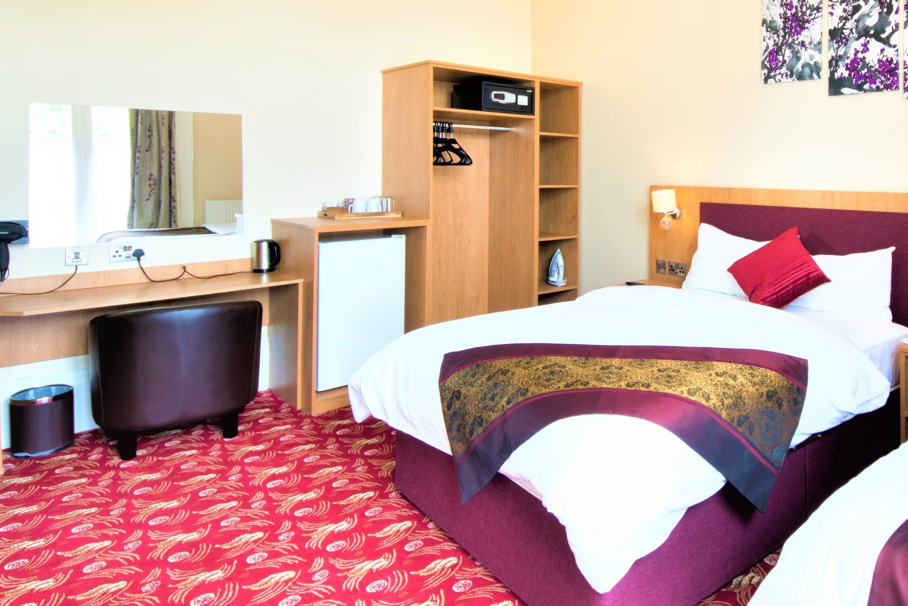 A hotel room with a bed, a desk, a chair, a wardrobe, and a mirror.