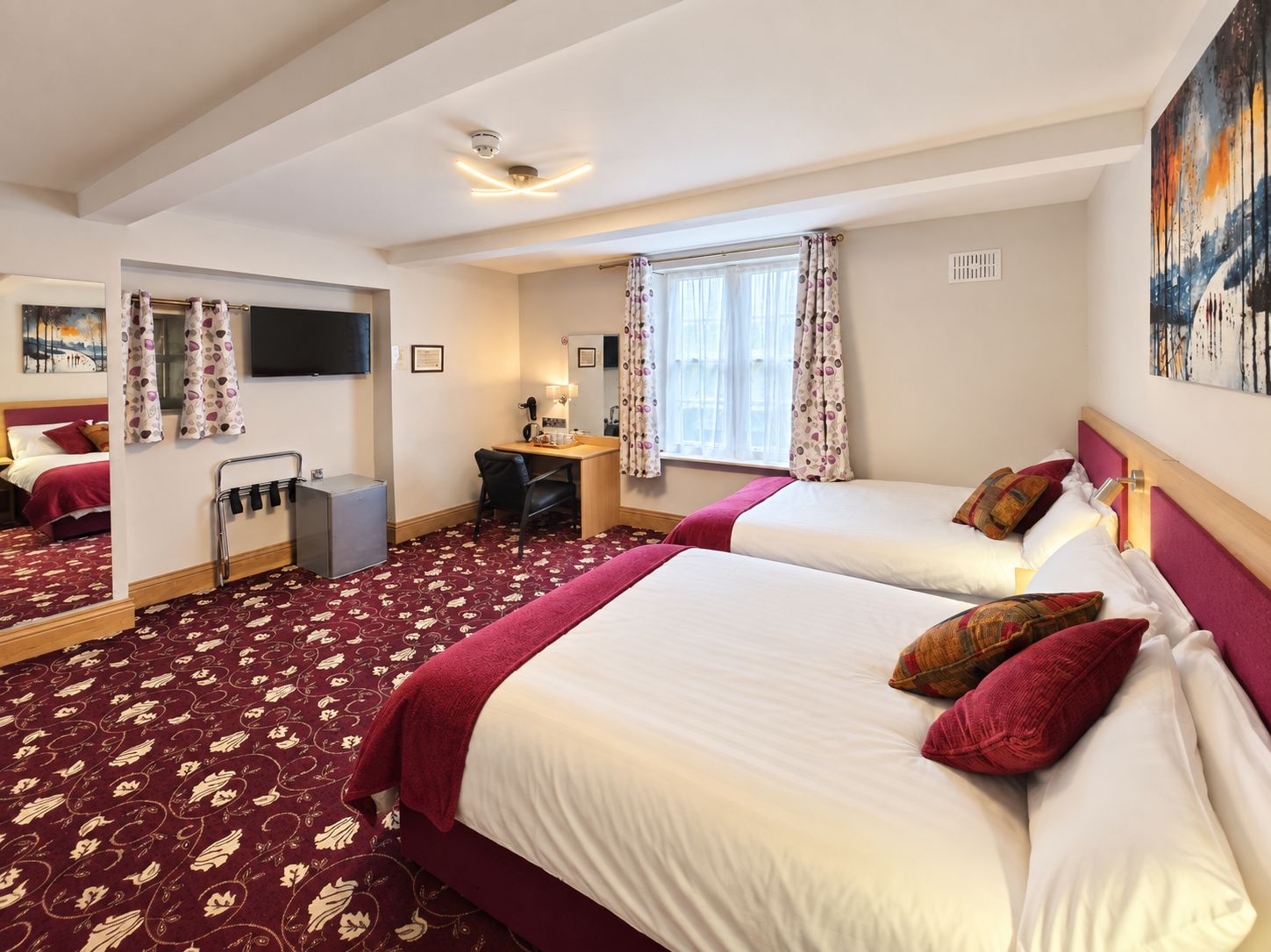 A hotel room with two beds, a desk, a chair, a television, and a window with curtains.