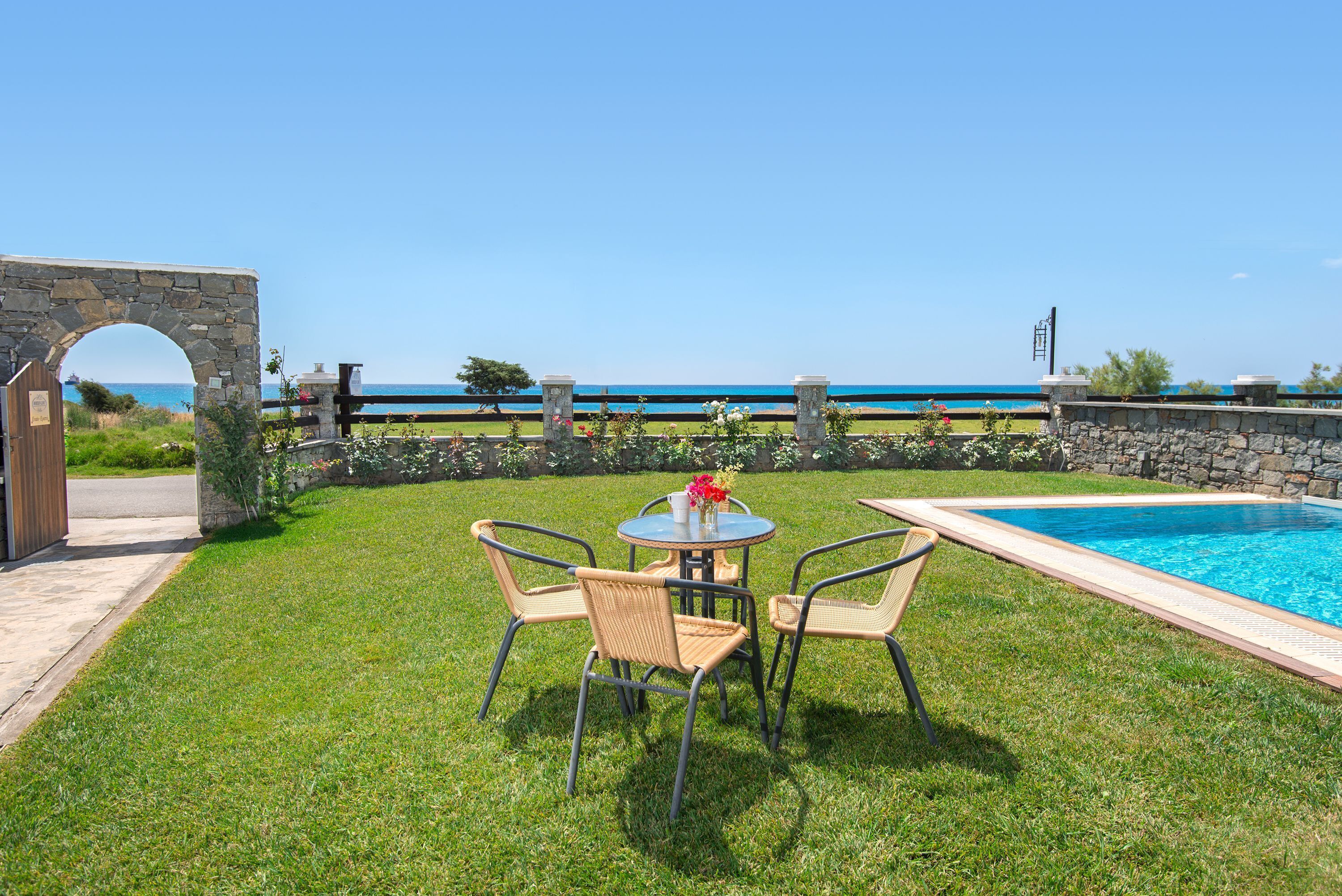 A poolside area with a stone archway, a round table with chairs, and a view of the ocean.