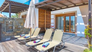 Una terraza de madera con cuatro tumbonas, una pérgola y un muro de piedra.