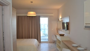 A hotel room with a bed, a desk, a chair, a television, and a view of the outside. - Argiro Village (Rhodes)