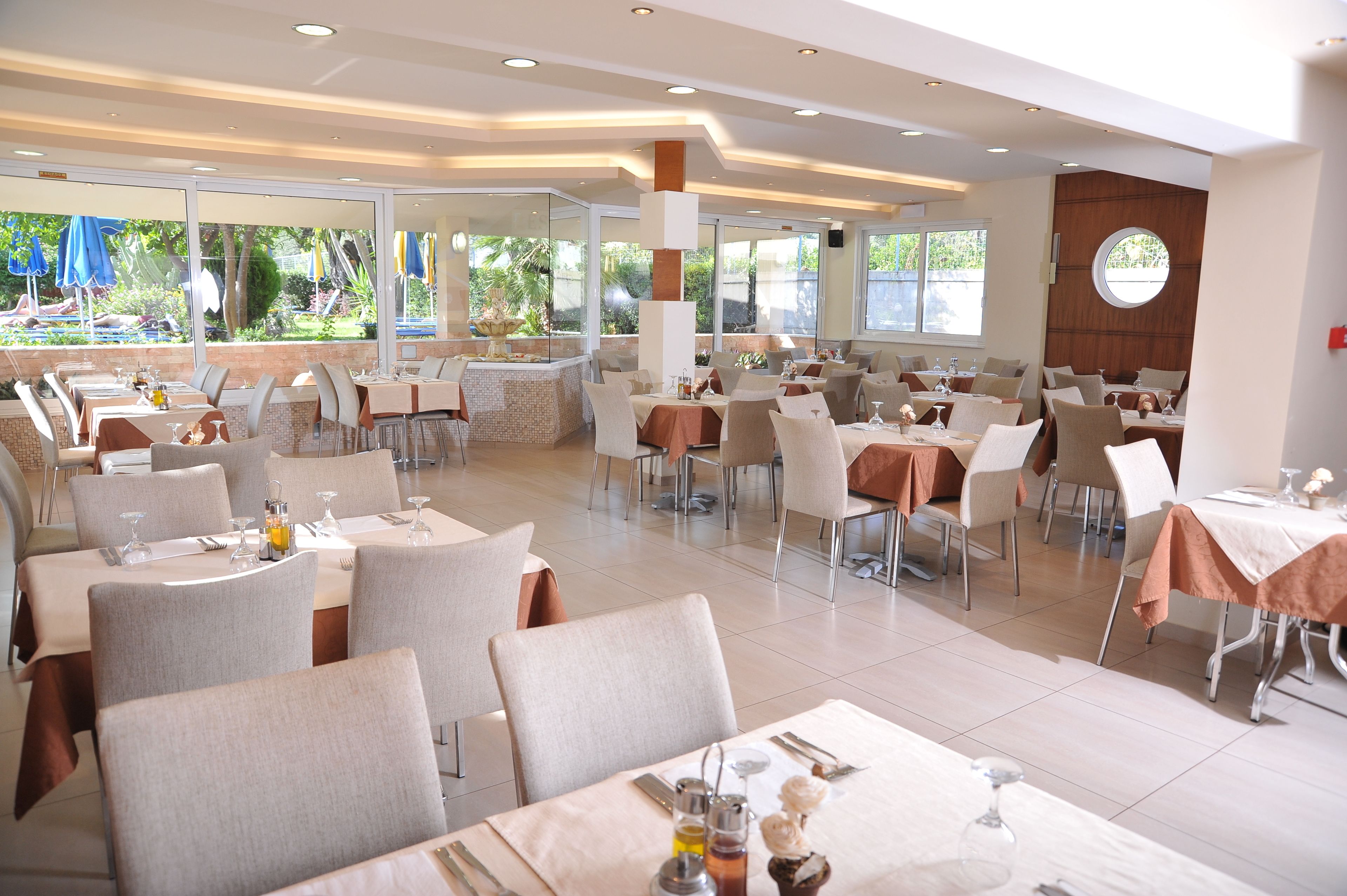A spacious restaurant with multiple tables and chairs, large windows offering a view of the outdoors, and a modern interior design.
