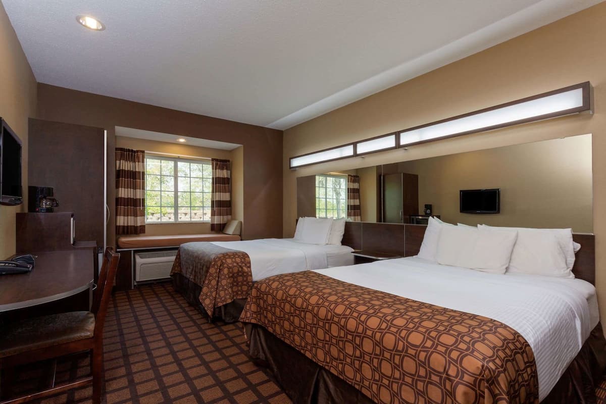 A hotel room with two beds, a desk, a chair, a TV, and a large window.