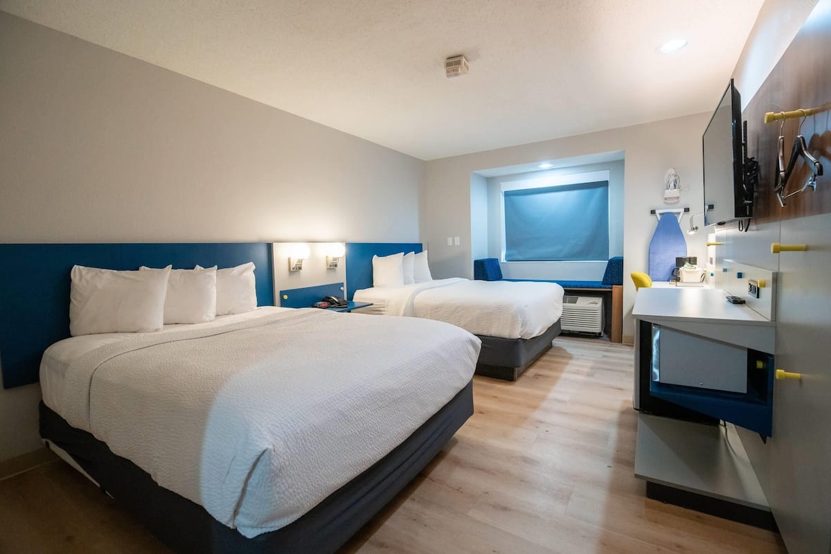 A hotel room with two beds, a desk with a chair, a window, and a mirror.
