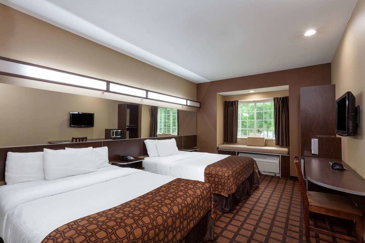A hotel room with two beds, a desk, a chair, a TV, and a window with curtains.