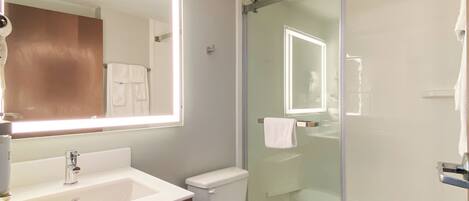 A modern bathroom with a large mirror, a sink, a toilet, and a glass-enclosed shower.