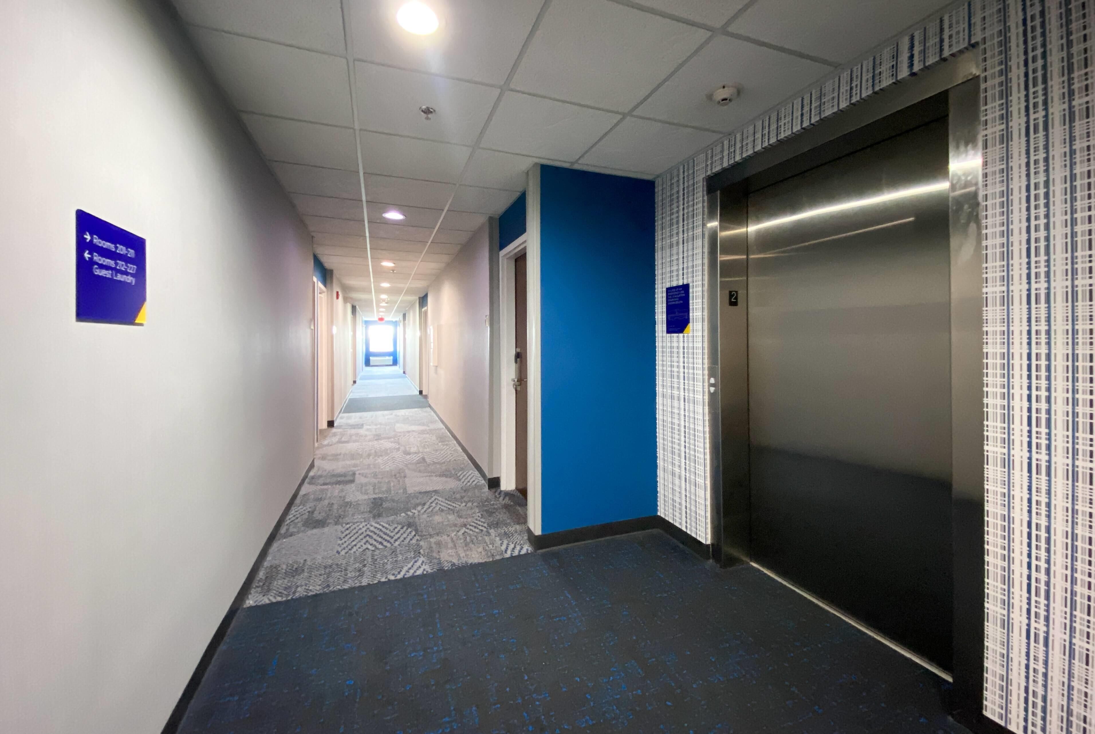 A hotel corridor with directional signs, an elevator, and a patterned carpet.