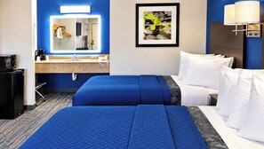 A hotel room with two beds, a desk, a microwave, and a sink.