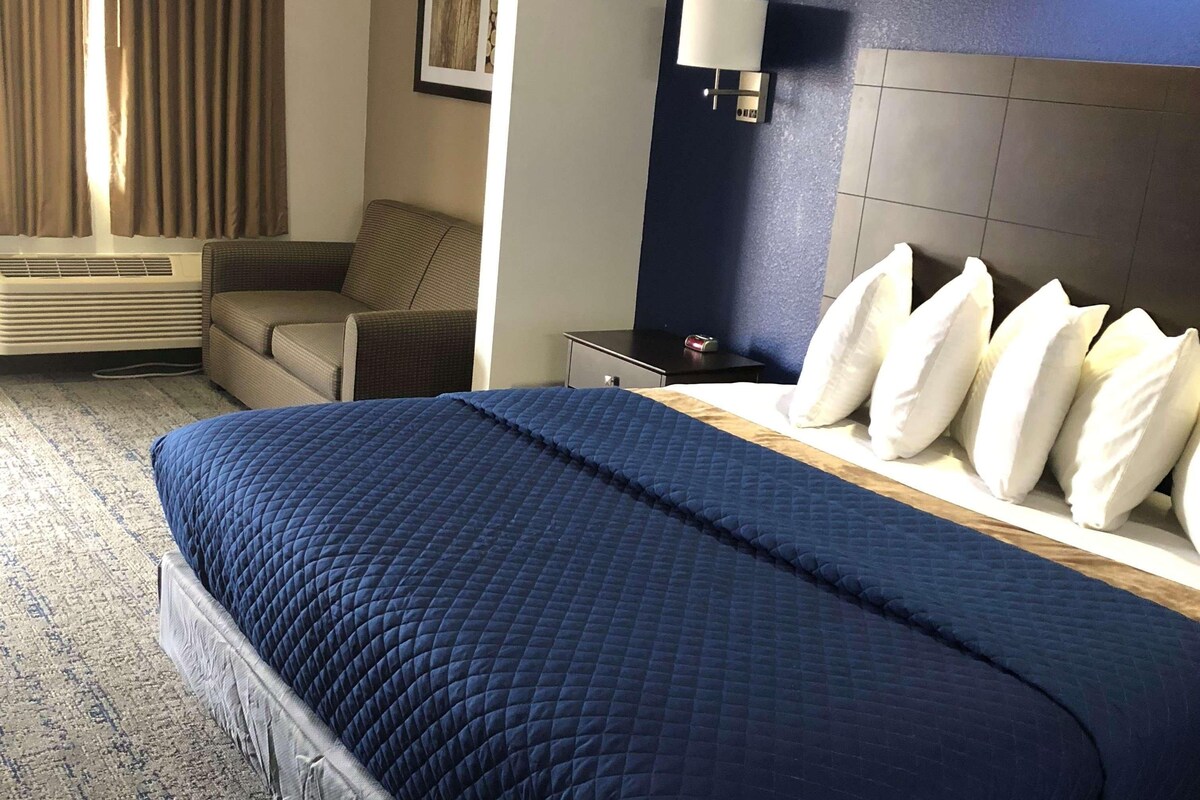 Une chambre d’hôtel avec un grand lit, une table de chevet, une lampe, une chaise et un tableau accroché au mur.