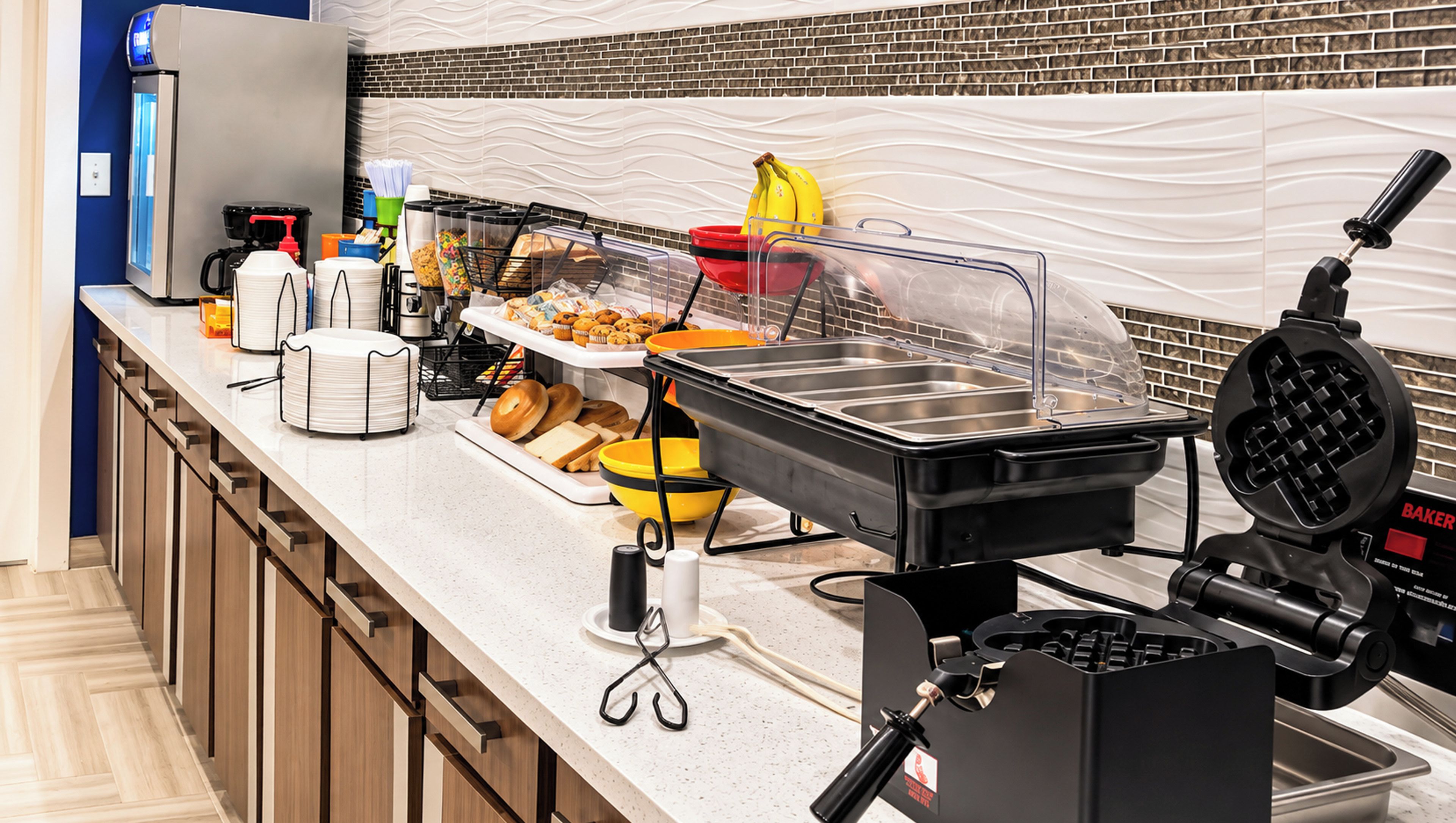 A buffet setup with various food stations, including a waffle maker, and a coffee machine.