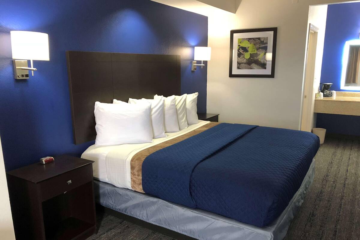 Ein Hotelzimmer mit einem großen Bett, einem Nachttisch, einer Wandlampe und einem gerahmten Bild an der Wand.