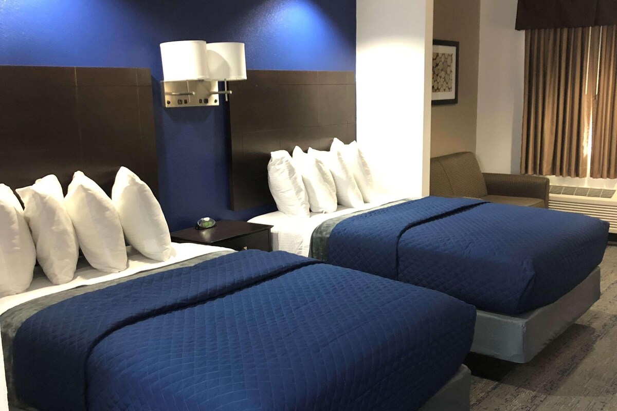 Une chambre d’hôtel avec deux lits, une table de chevet avec une lampe, un canapé et une fenêtre avec des rideaux.