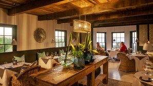 Un comedor con mesas de madera, sillas de mimbre y ventanas amplias.