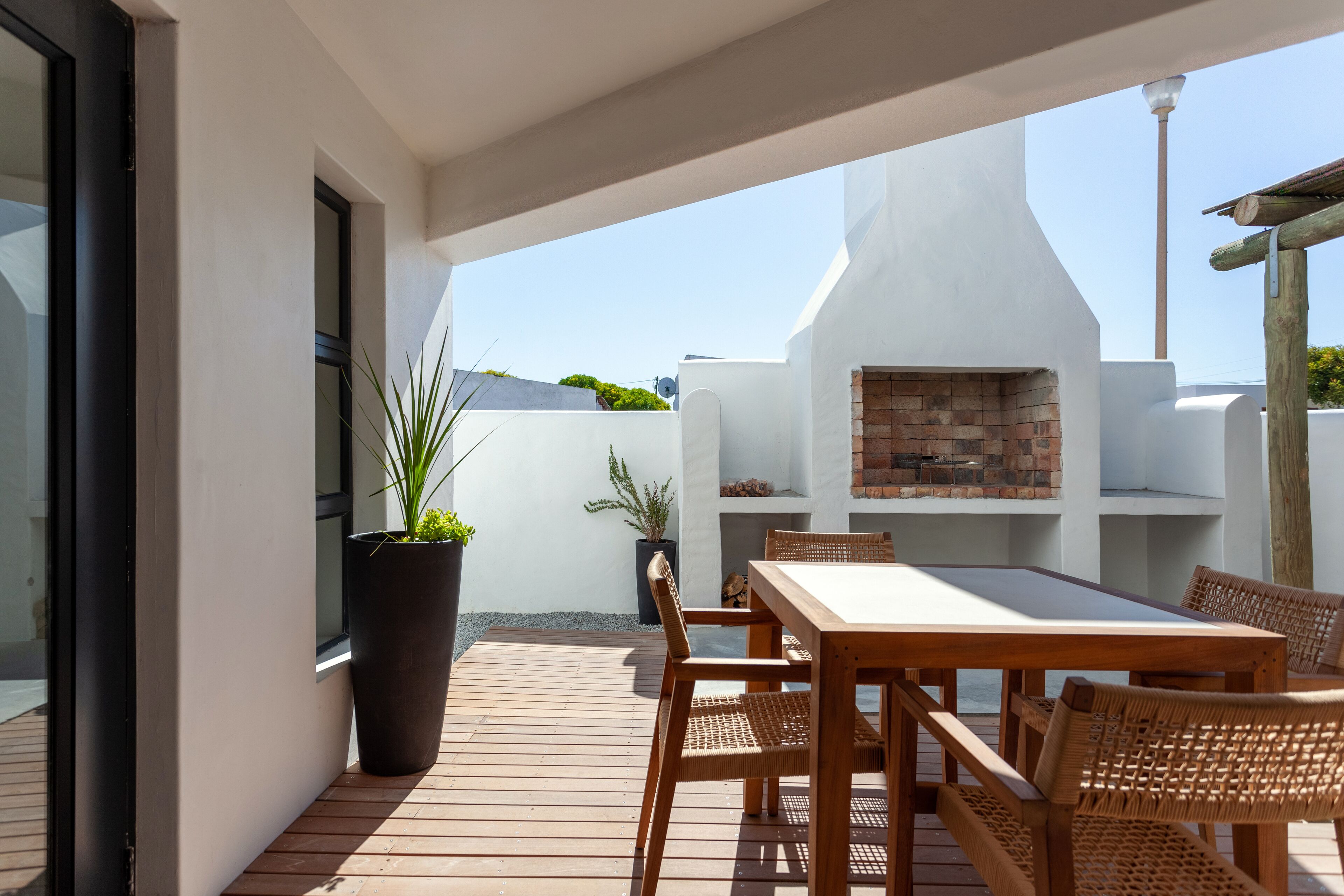An outdoor patio with a wooden table and chairs, a brick oven, and potted plants.