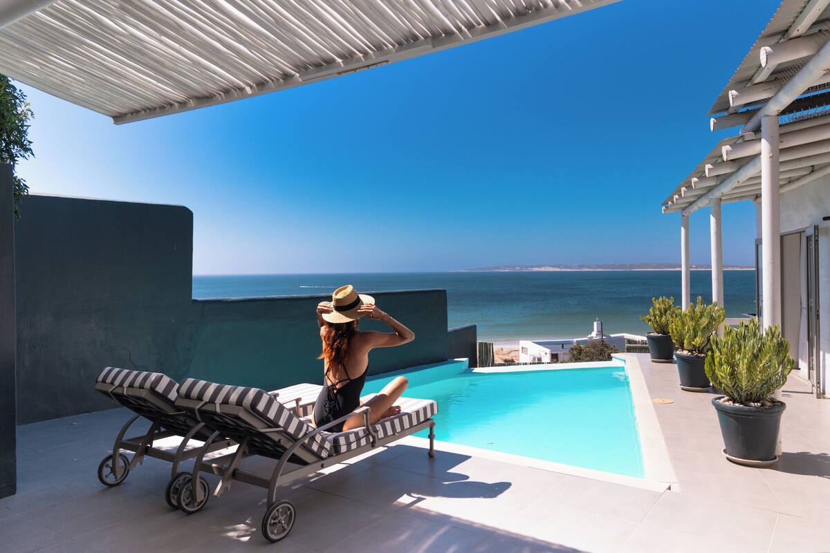 Zona de piscina con sillones de descanso y una mujer sentada junto a la alberca.