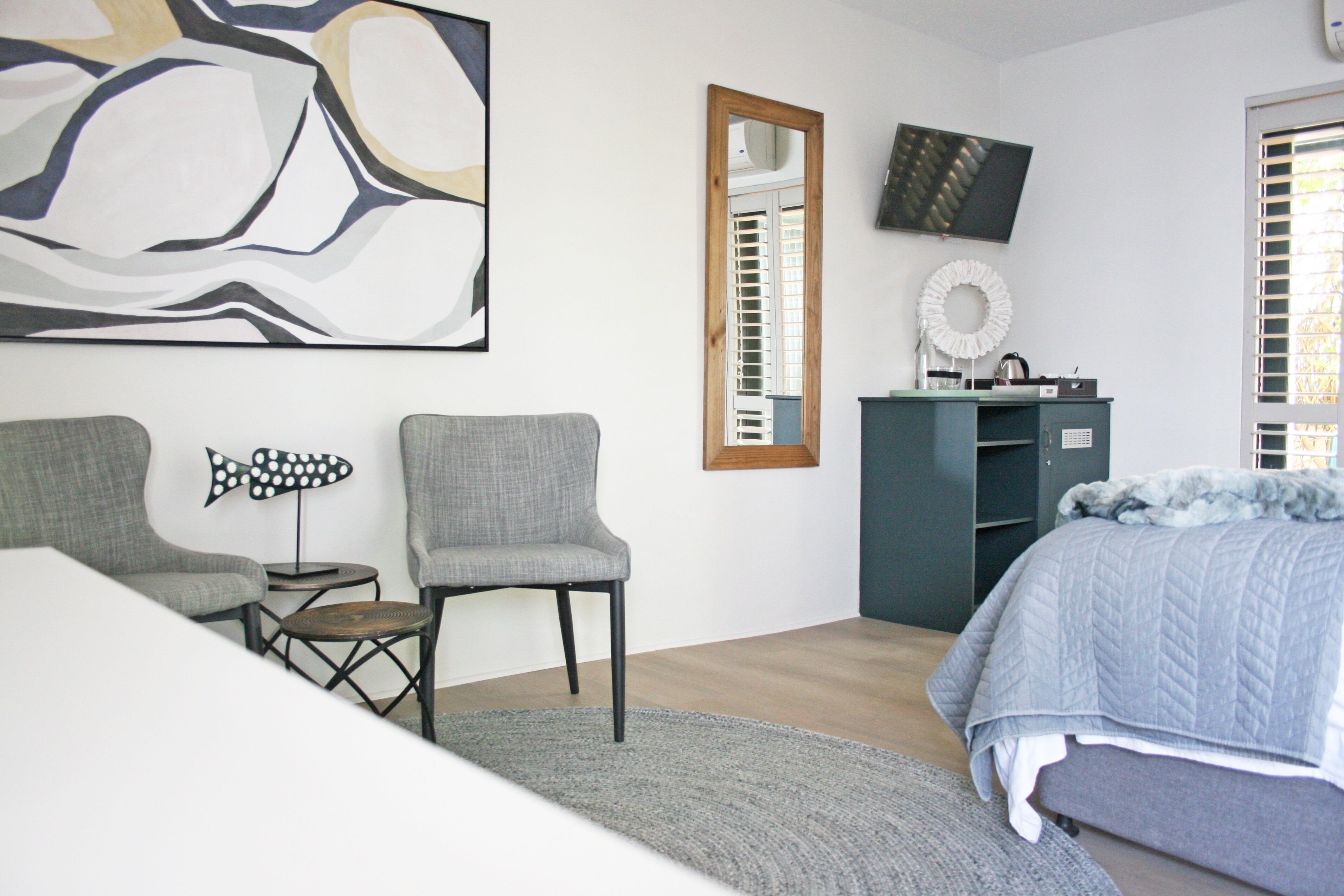 A bedroom with a bed, two chairs, a small table, a mirror, a TV, and a decorative wreath.