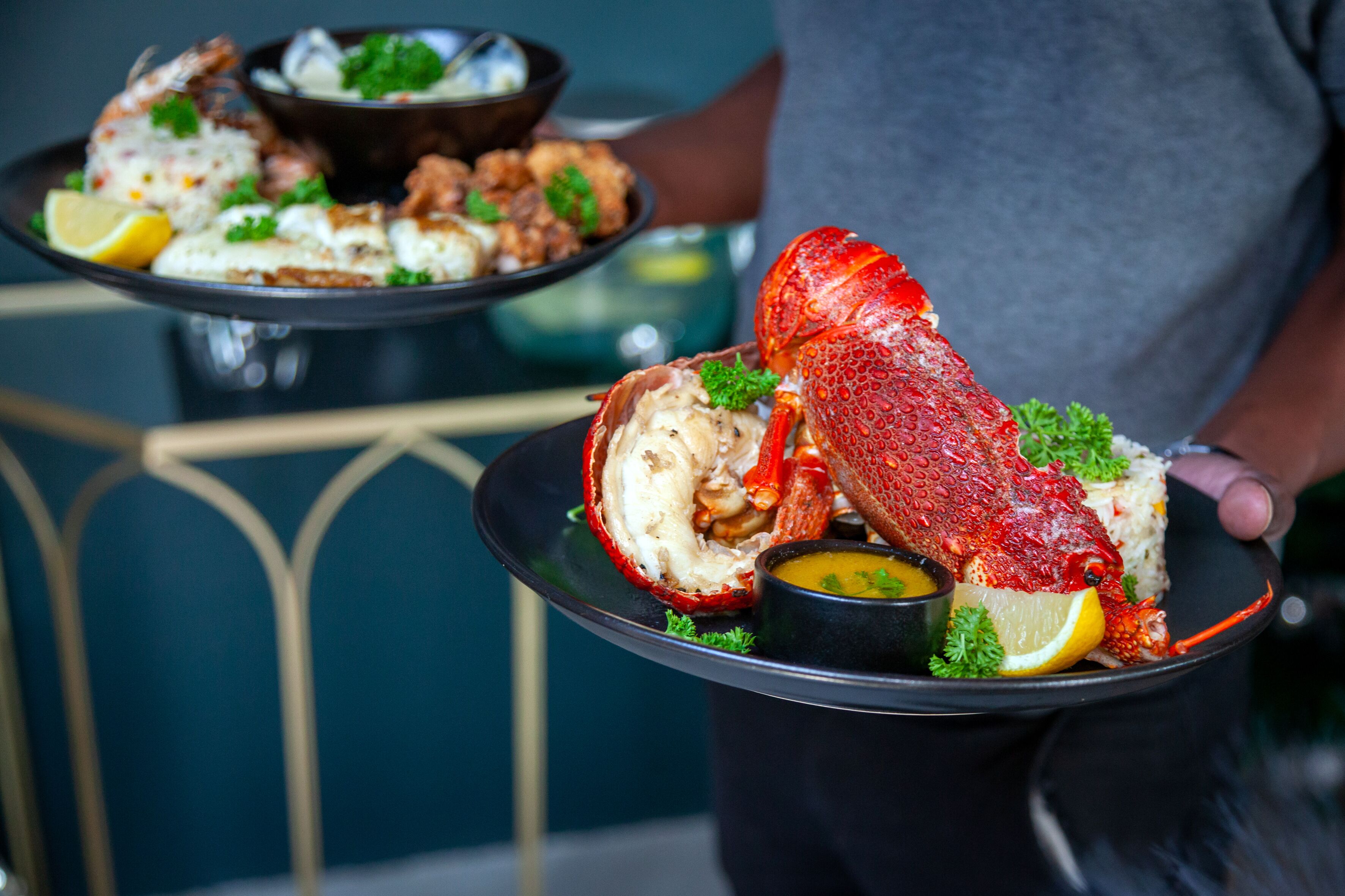 A person holding a lobster tail with lemon and parsley garnish.