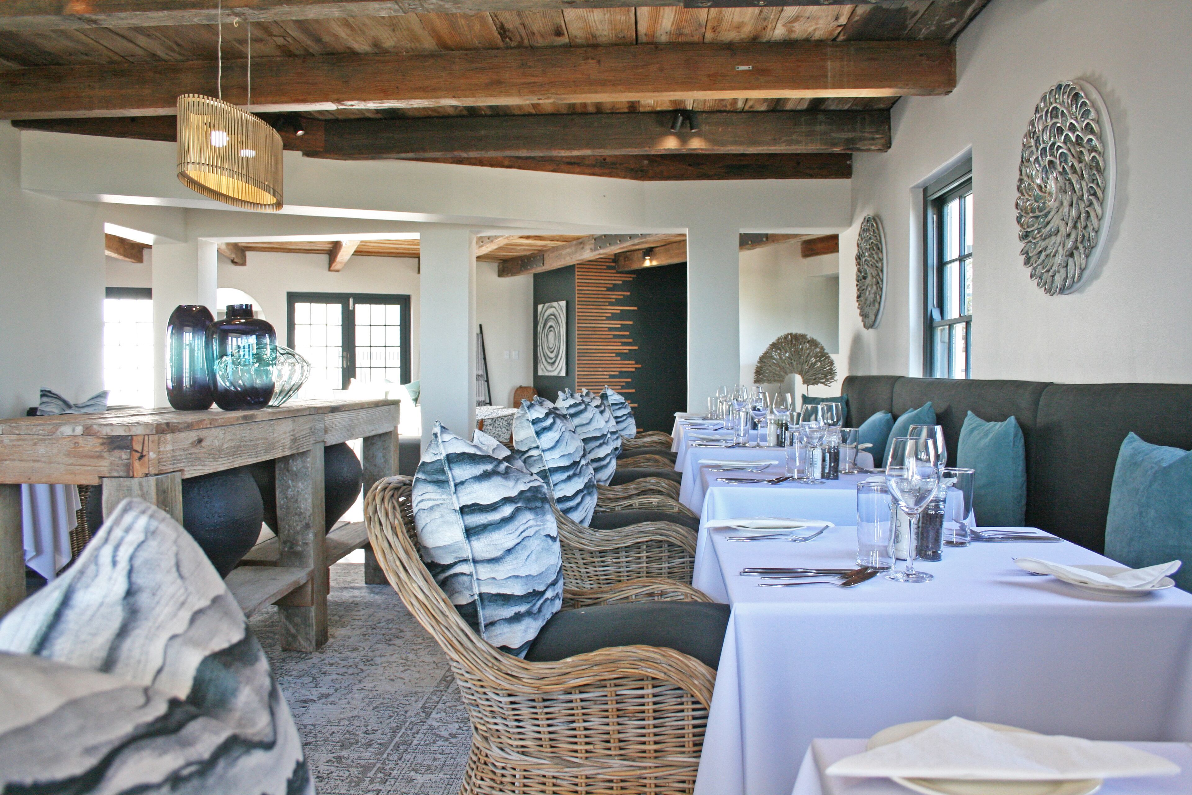A dining area with wicker furniture, white tablecloths, and a rustic ceiling.