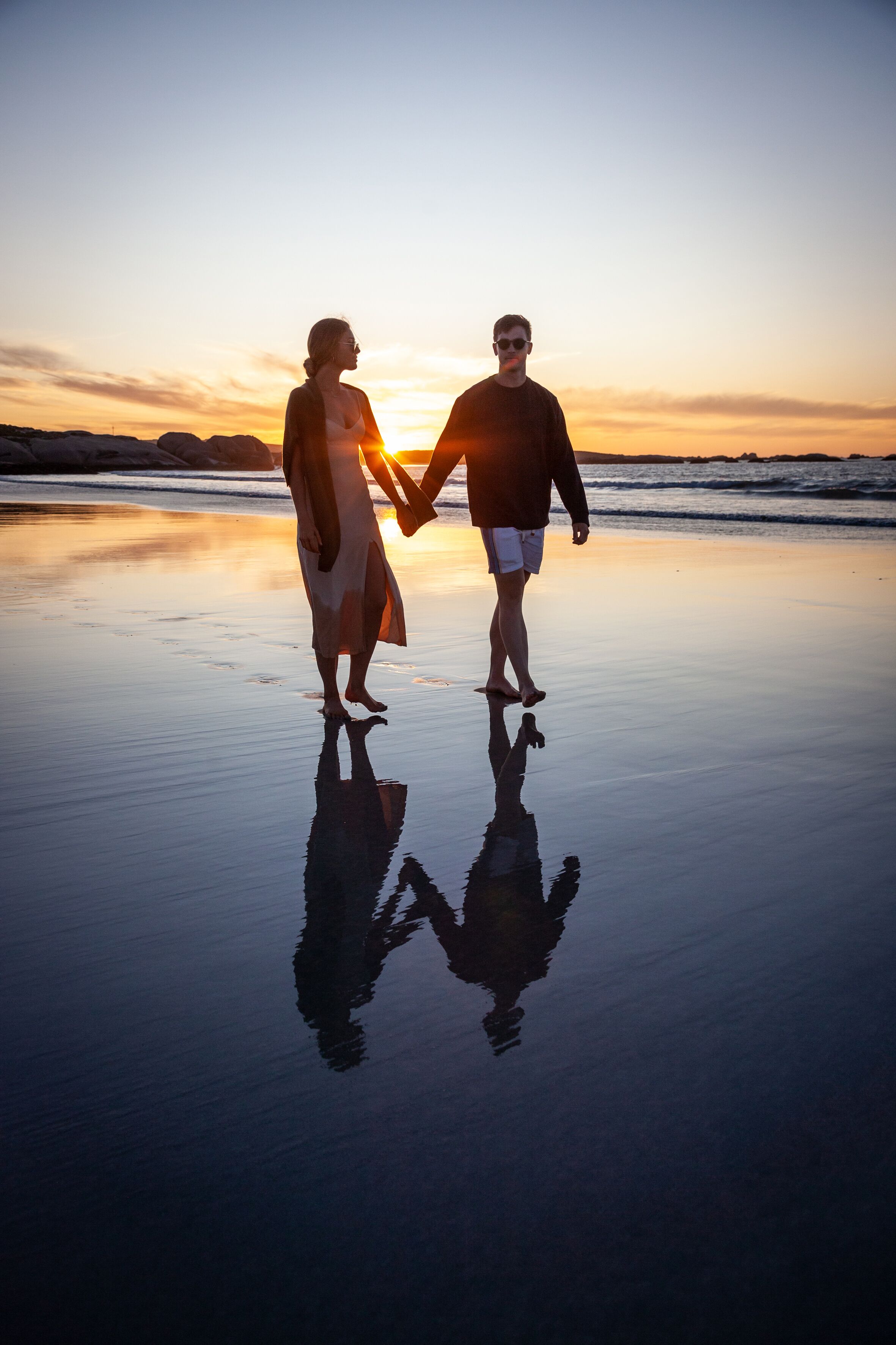 A couple holding hands on a beach at sunset.
