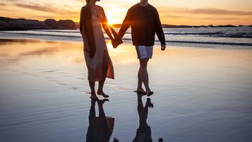 A couple holding hands on a beach at sunset.