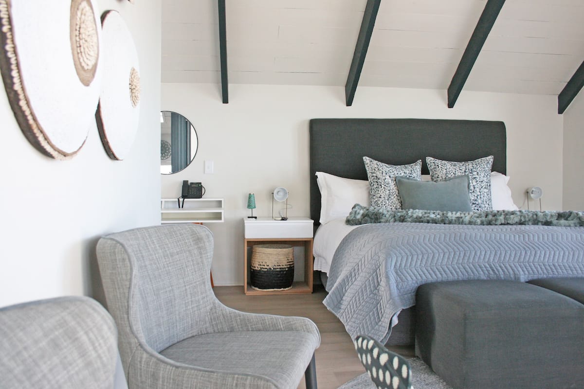 Un dormitorio con cama, dos sillones, una mesita de noche, un espejo y decoración en la pared.