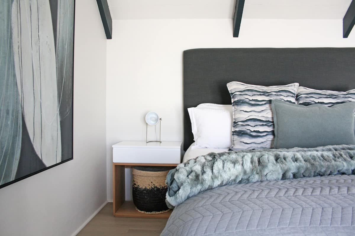 Un dormitorio con cama, mesita de noche, lámpara y una obra de arte colgada en la pared.