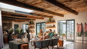 Una sala de estar moderna con techo alto, vigas de madera y un ventanal grande. Hay dos sofás, una mesa de centro y una mesita auxiliar.