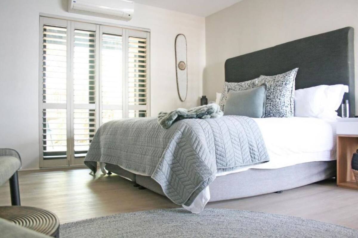 Un dormitorio con cama, mesita de noche, silla, ventana con persianas y aire acondicionado instalado en la pared.
