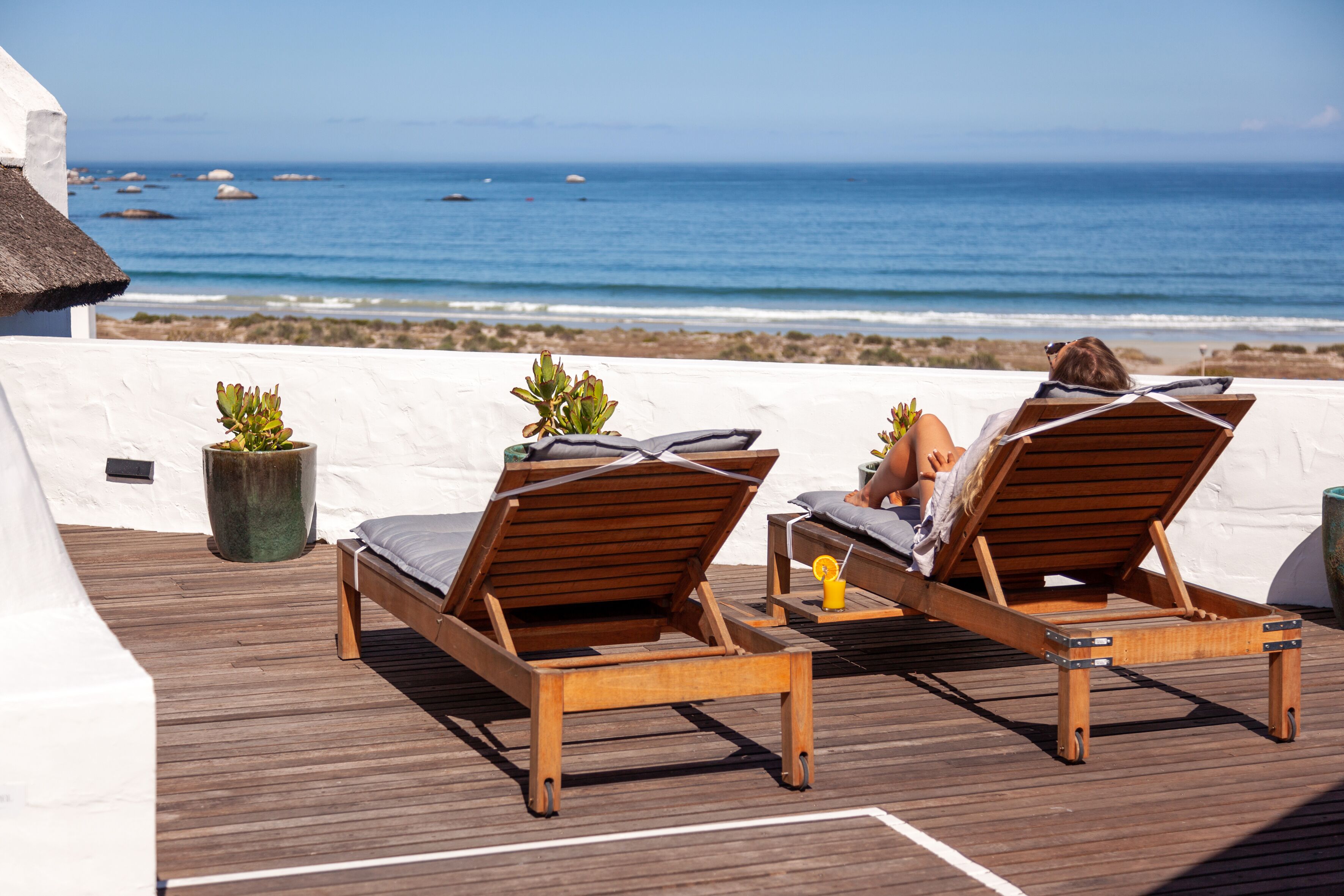 Deux fauteuils de jardin en bois, placés sur une terrasse en bois, offrent une vue sur l’océan.