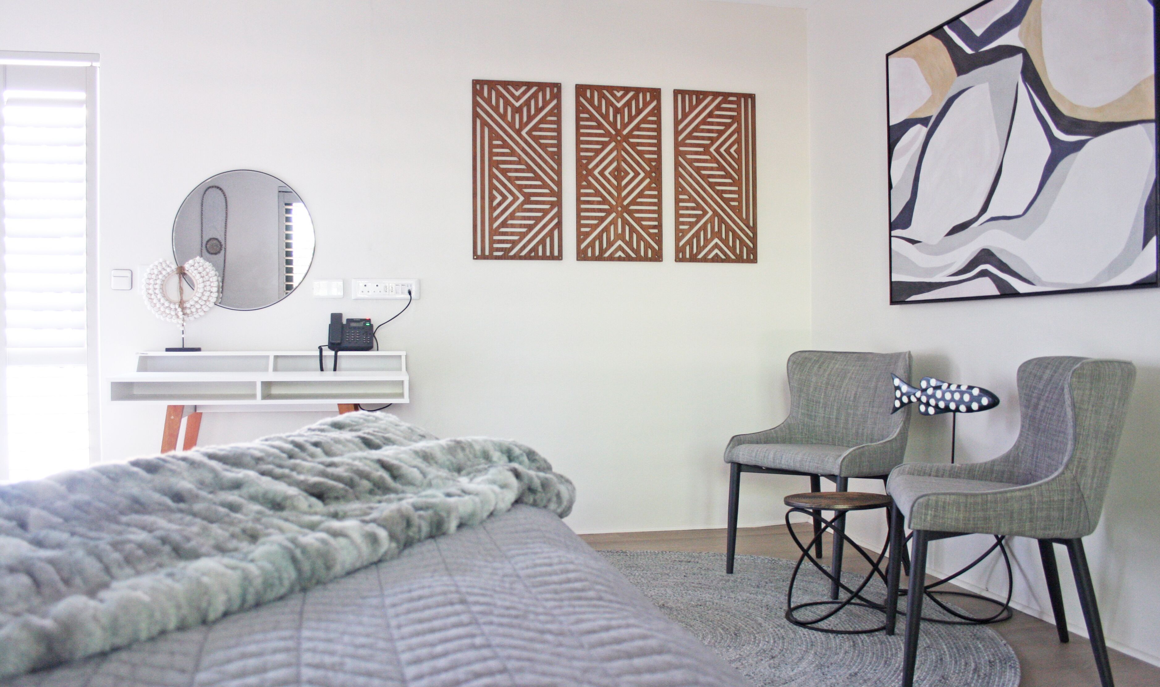 A modern bedroom with a bed, two chairs, a desk with a phone, and decorative wall art.